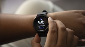 A person is adjusting a smartwatch on their wrist with their other hand. The smartwatch screen displays the current time, sleep duration, and includes a moon icon, possibly indicating sleep tracking.