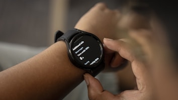 A person is wearing a smartwatch on their wrist, with the display showing health-related information such as blood oxygen levels and time under 90%. The person is interacting with the watch, touching the screen with their fingers.
