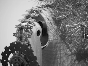 An intricate assembly of mechanical parts including gears and chains set against a textured backdrop, with metallic, spiky structures extending outward.