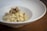 A plate of creamy risotto garnished with slices of truffle is elegantly presented in a deep white bowl, placed on a wooden table.