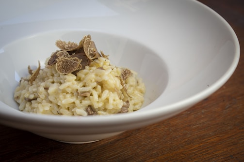 A delicate mushroom risotto topped with thinly sliced black trumpets and a sprinkle of fresh herbs in a minimalist white bowl.