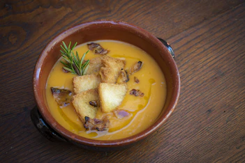 A warm ceramic bowl filled with a creamy seasonal vegetable soup garnished with fresh parsley.