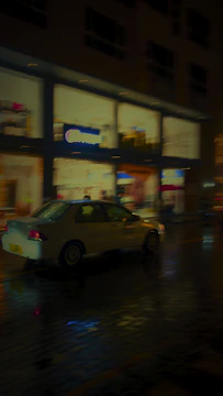 A candid image of a car navigating through bustling city streets at dusk, lights reflecting off wet pavement.