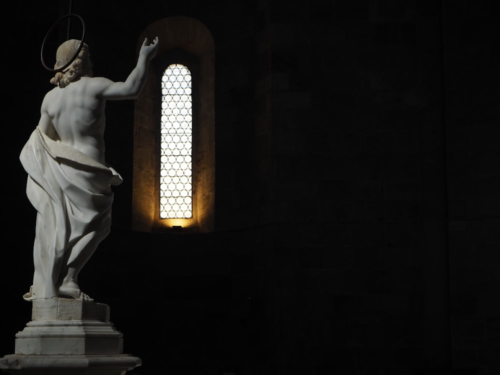 a statue in a dark room with a window behind it