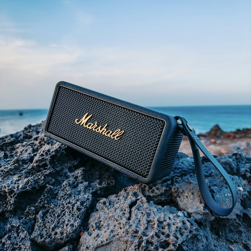 A Marshall wireless speaker with amp-inspired grille and control knobs, photographed outdoors on rock