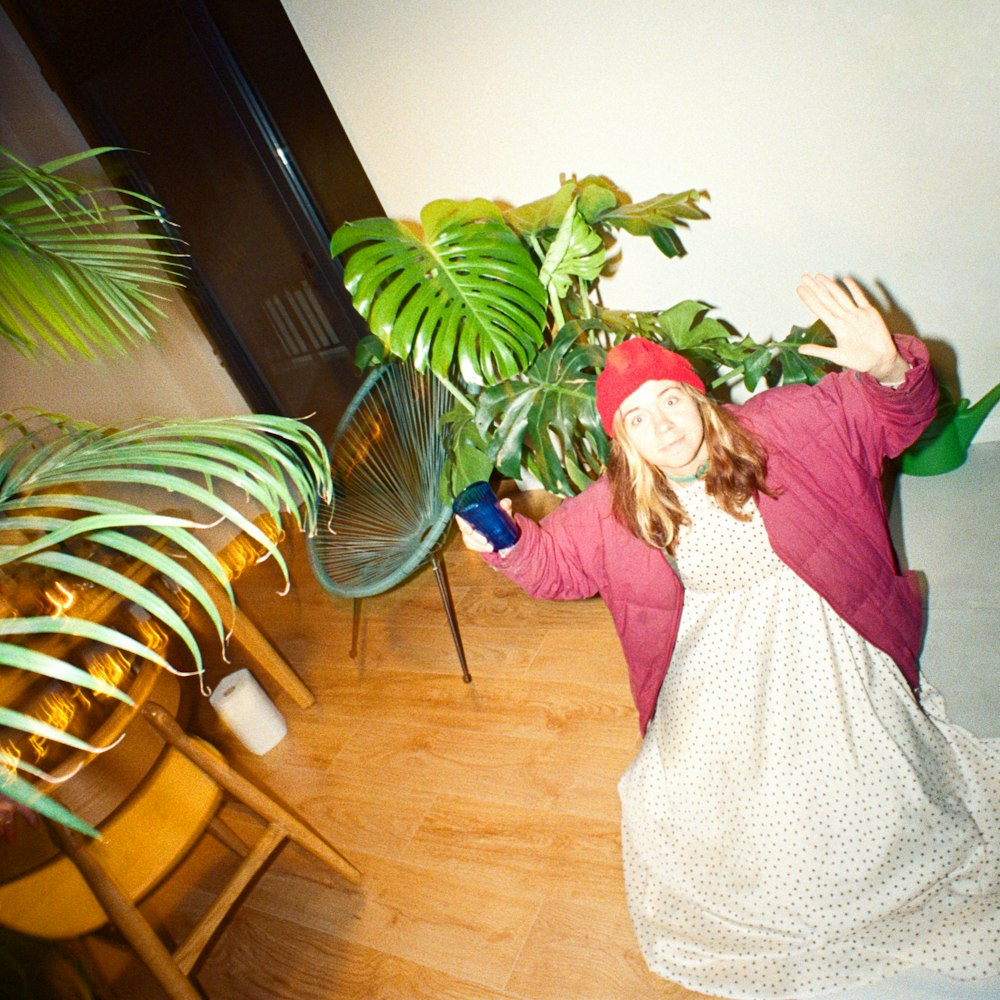 a young girl in a dress and hat standing in front of a potted plant