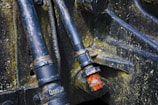 Dark metal pipes and bolts with evident rust and wear, mounted on an industrial or mechanical structure. The metal surfaces display signs of aging and corrosion, showing patches of yellowish-green mold or oxidation.