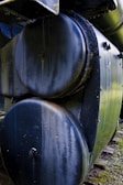 Close-up view of a large metal boiler or tank with a weathered surface. The cylindrical body shows signs of rust and wear, while bolts and rivets are visible along the edges.