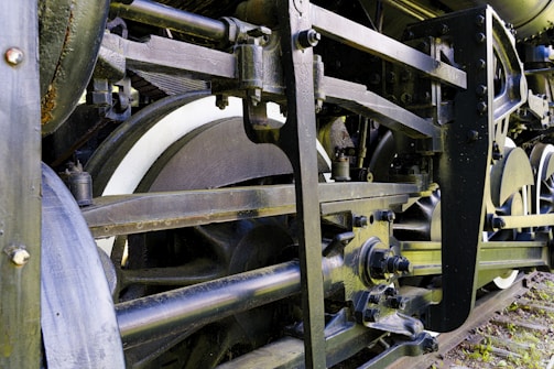 Complex machinery is depicted, showcasing the intricate details of a train's mechanical system with visible gears and connecting rods. The metal components are robust and industrial, emphasizing the engineering design of an old locomotive.