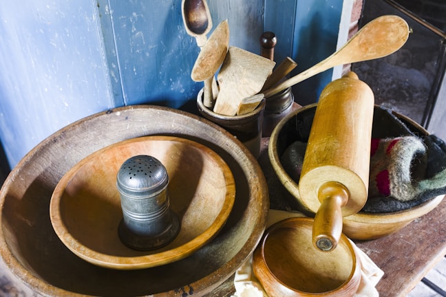 A collection of well-loved kitchen gadgets and baking tools arranged on a warm-toned countertop with a backdrop of mountain scenery.