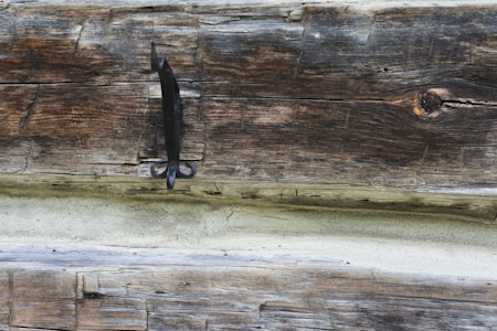 A weathered wooden plank with visible grain and texture, featuring a metal handle or latch attached.