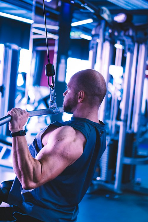 Client performing a cable pulldown exercise under blue gym lighting