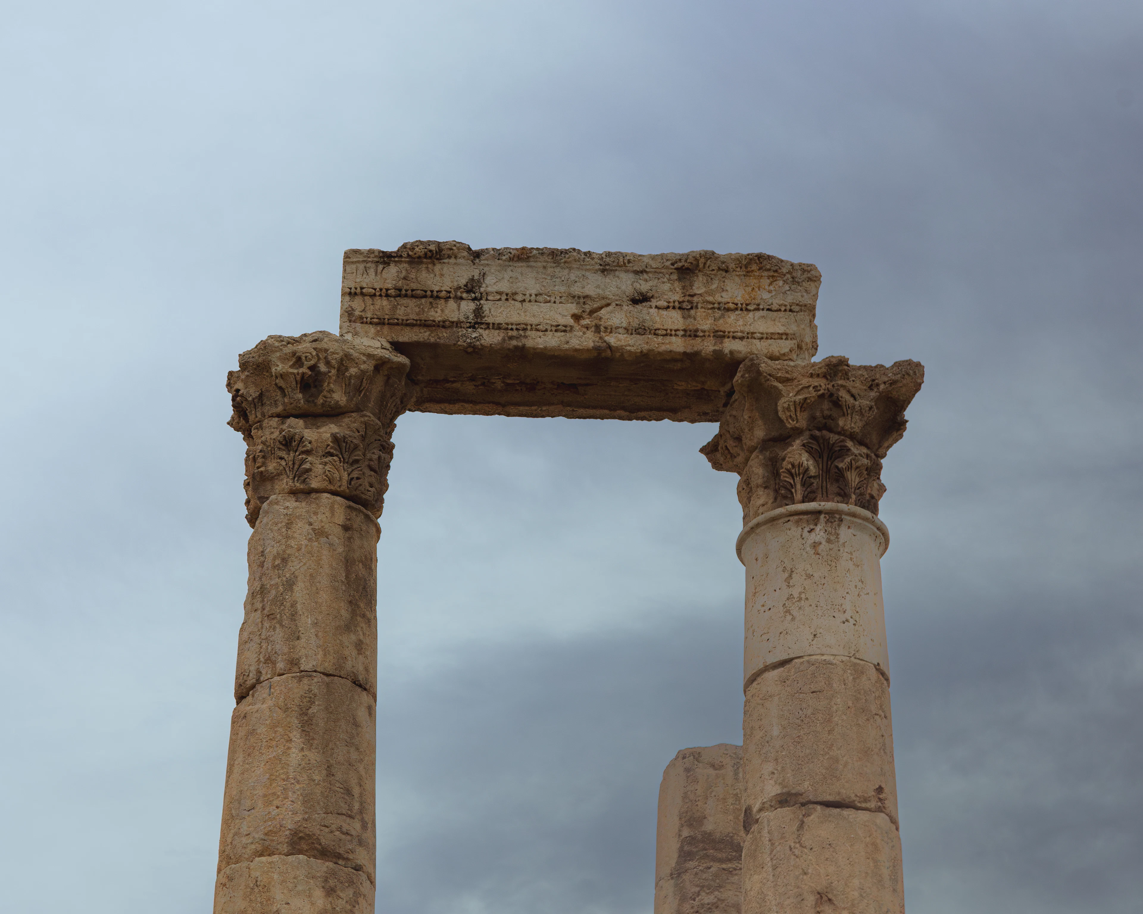 Two towering ancient columns at Amman's Citadel rise against a dramatic cloudy sky.