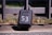 A black lock box with the number 53 written on it in white is secured to a metal gate. The box is positioned against a stone surface, with a grassy area visible in the blurred background.