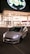 A sleek white car with prominent front lights is parked in front of a brightly lit modern building at nighttime. The building has large glass windows and a sign reading 'Pogliano Milanese.' The glowing brand sign, 'globo,' is prominently displayed above the entrance.