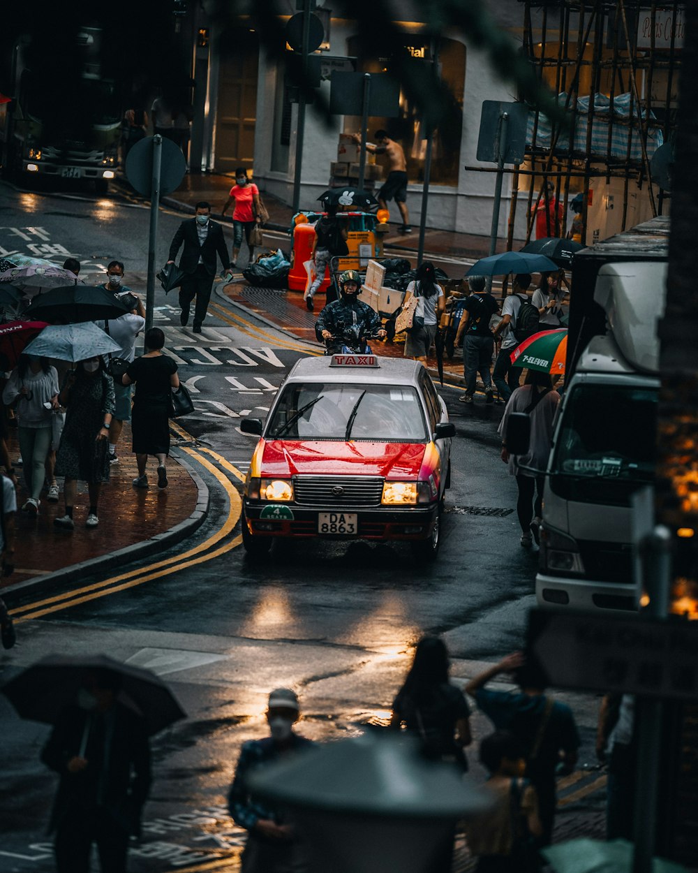 a red car driving down a rain soaked street