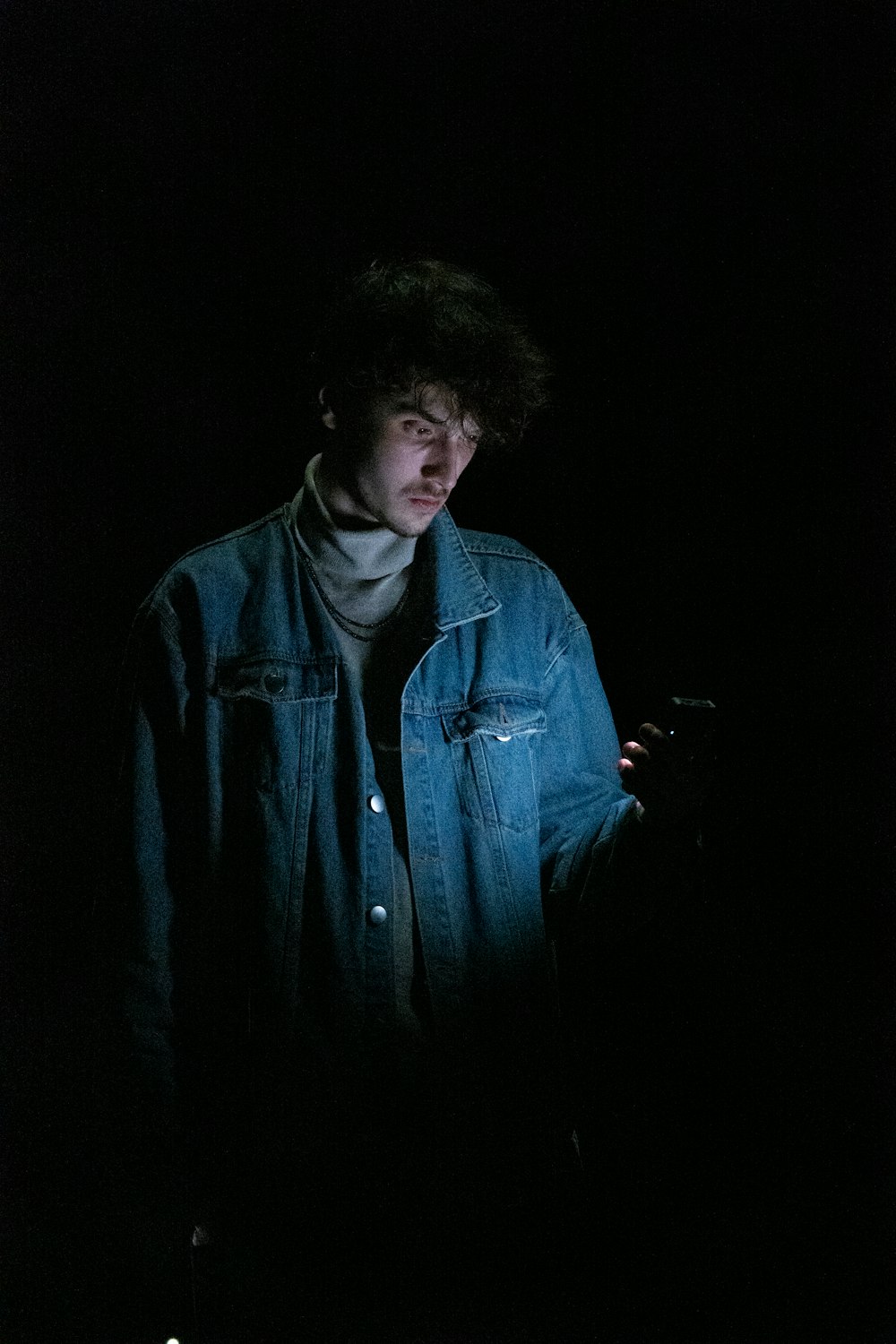 a man standing in the dark looking at his cell phone
