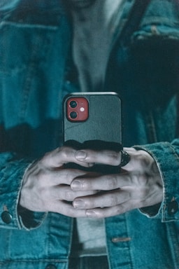 A close-up of hands typing on a smartphone with a denim jacket sleeve visible.