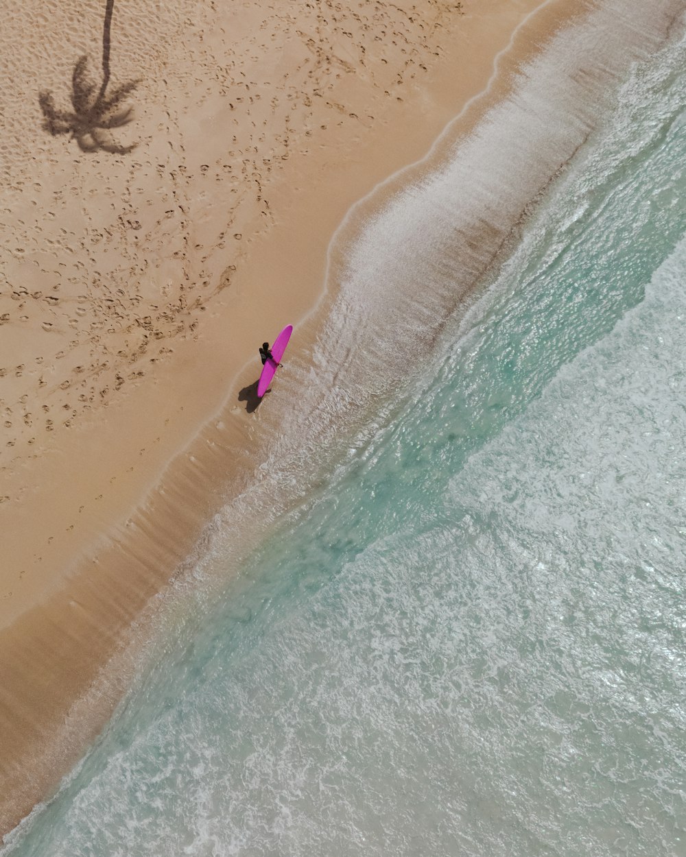 une vue aérienne d’une personne sur une plage avec une planche de surf