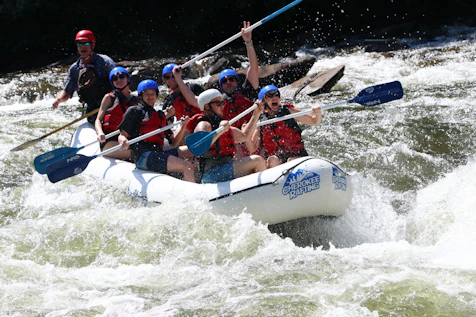 Group of adventurers navigating white water rapids in a raft on a sunny day.