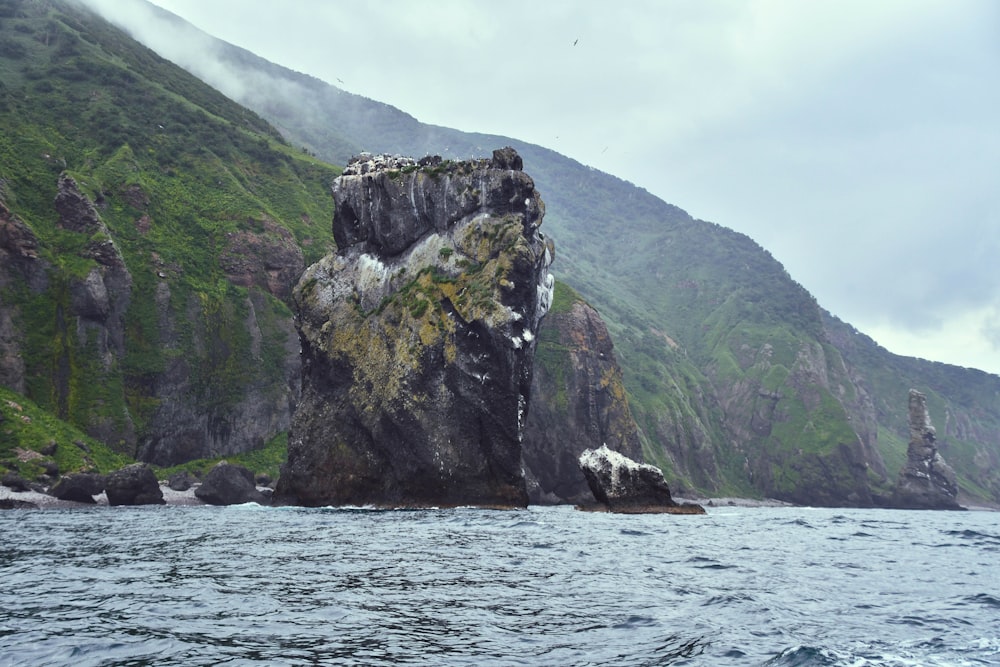 a large rock sticking out of the ocean next to a mountain