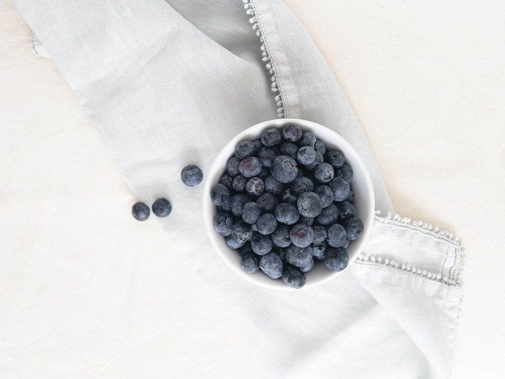a white bowl filled with blueberries on top of a white cloth