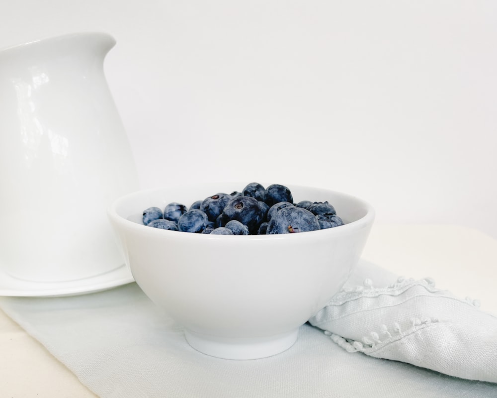 a bowl of blueberries next to a pitcher of milk