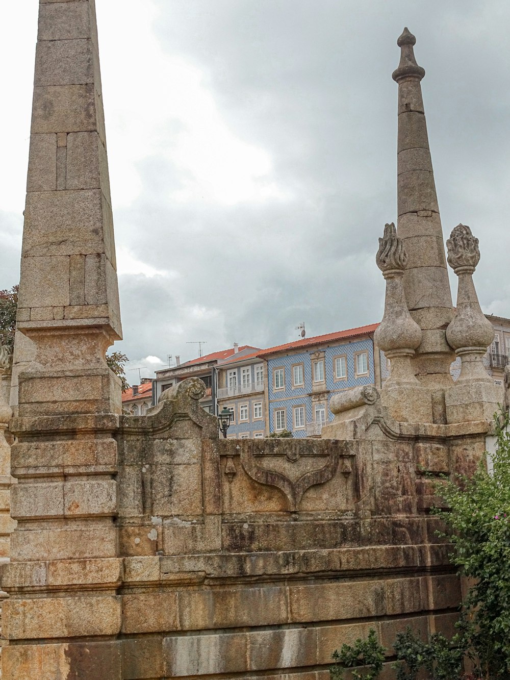 Ein hoher Steinobelisk sitzt neben einer Steinmauer