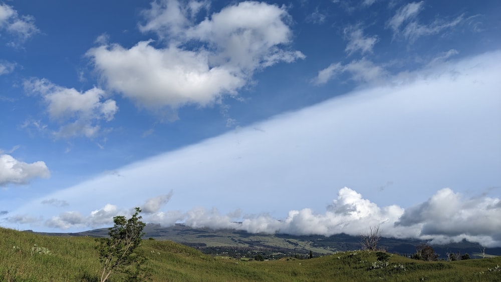 a grassy hill with clouds in the sky