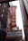 A large vertical marquee sign with the word 'CHICAGO' in bold letters hangs from a classic theater building. The sign is red with white letters and is bordered with lights. Below, there is a board listing upcoming events and dates, including shows by Iliza, Corey Holcomb, and Nikki Glaser. Surrounding the marquee are historic brick and stone buildings, hinting at an urban setting.