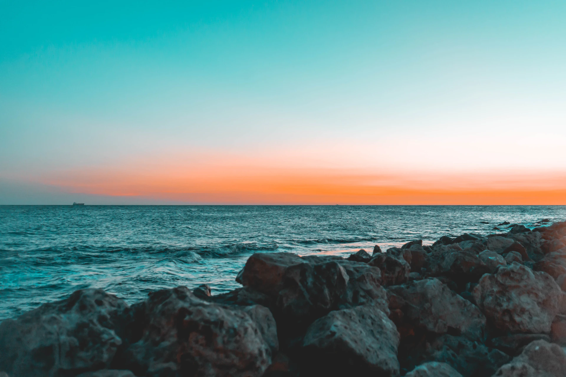 the sun is setting over the ocean and rocks
