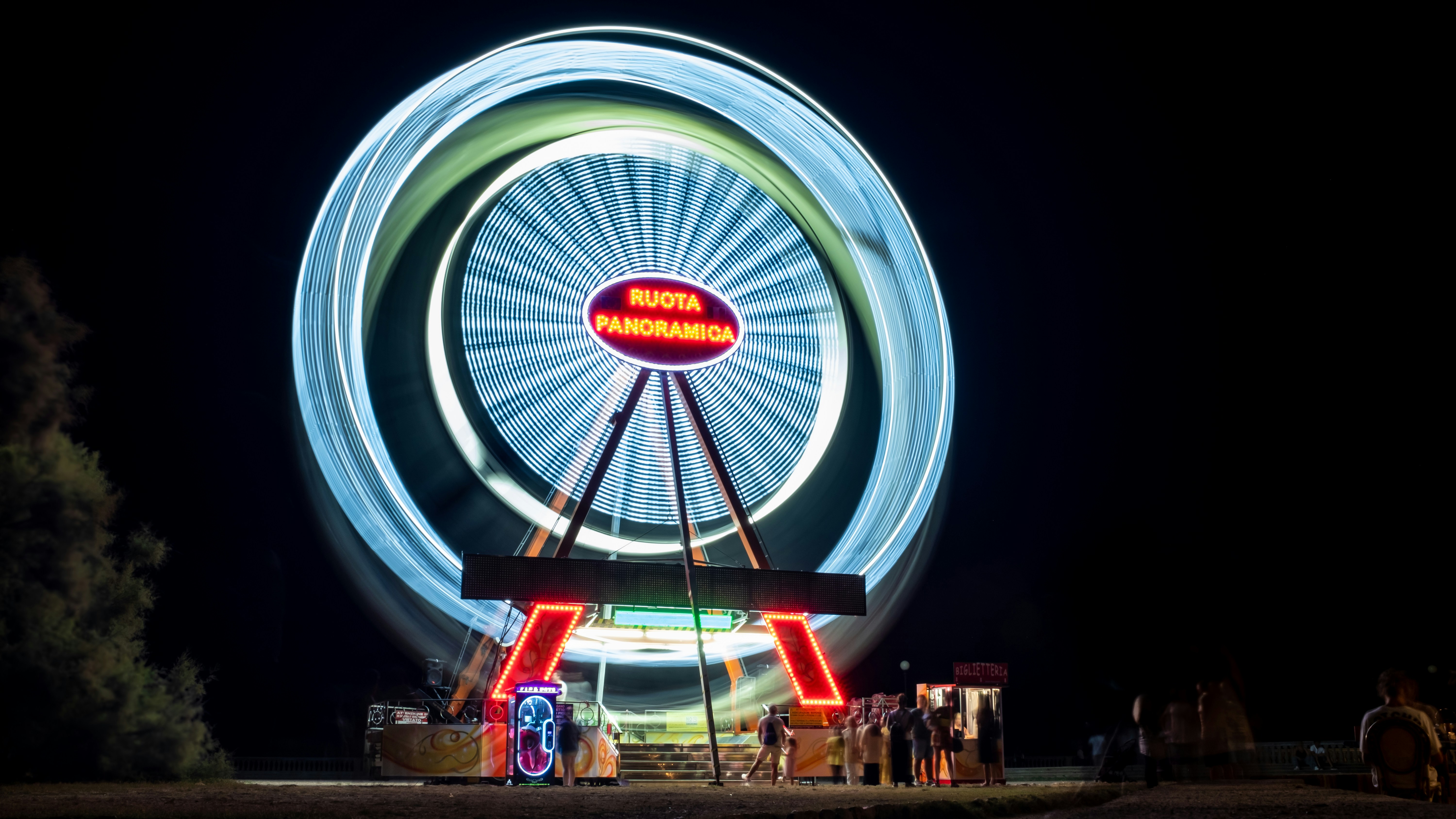 a ferris wheel at night with people standing around it