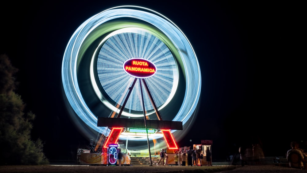 uma roda-gigante à noite com pessoas em pé ao seu redor