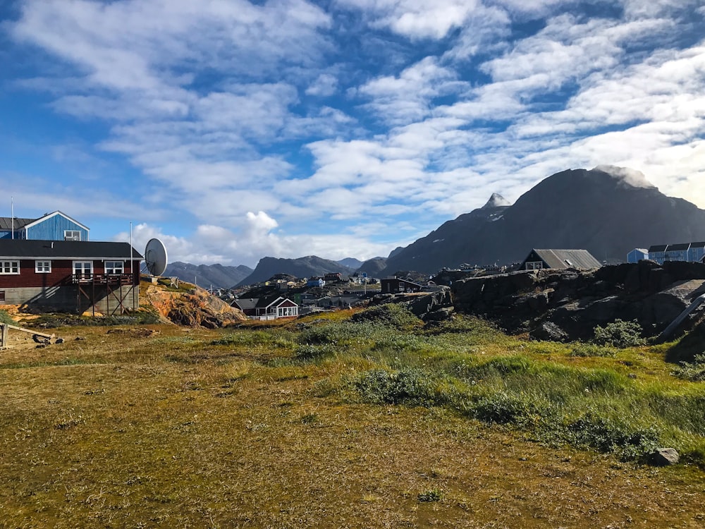 a grassy field with houses and mountains in the background