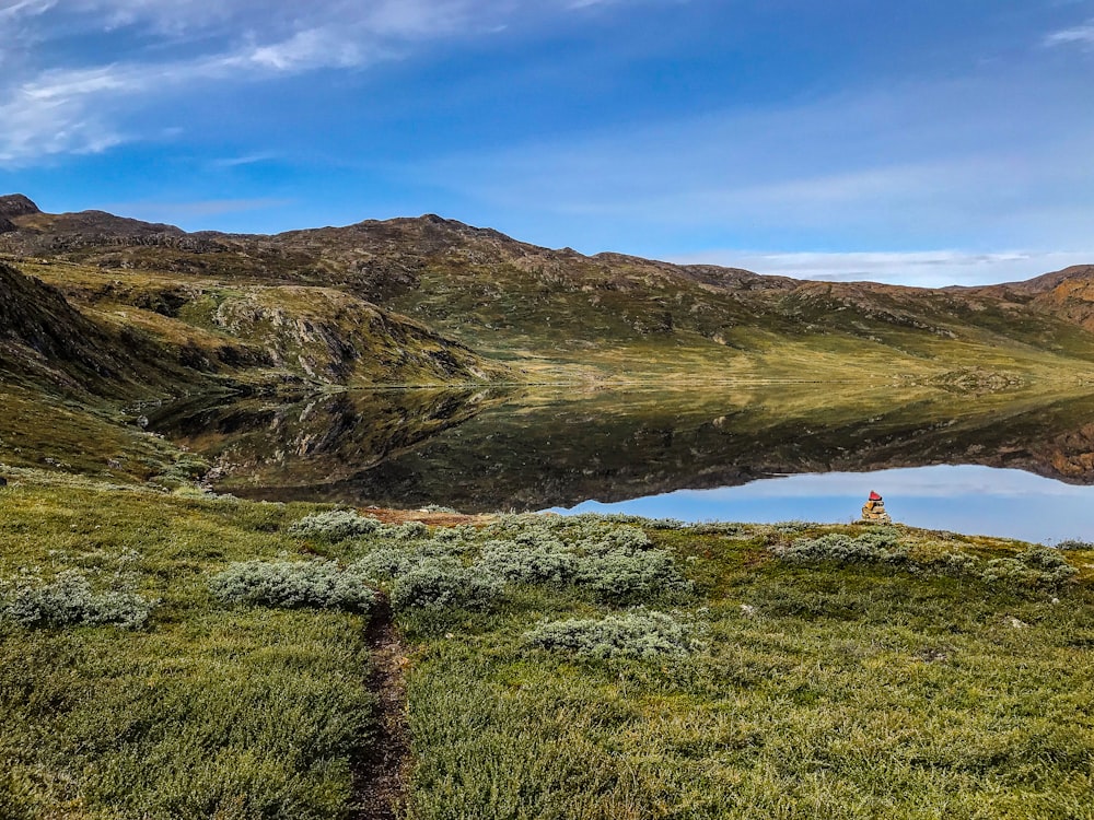 a person standing on top of a grass covered hill next to a lake