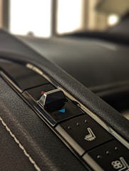 A close-up of a car's interior control panel featuring a seat adjustment switch with blue and red indicators on a textured black surface.