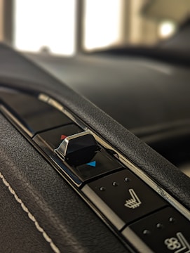 A close-up of a car's interior control panel featuring a seat adjustment switch with blue and red indicators on a textured black surface.