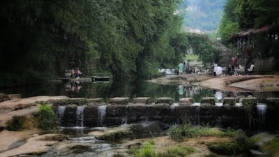 Peaceful riverside scene where community members gather amidst dense greenery and calm waters.