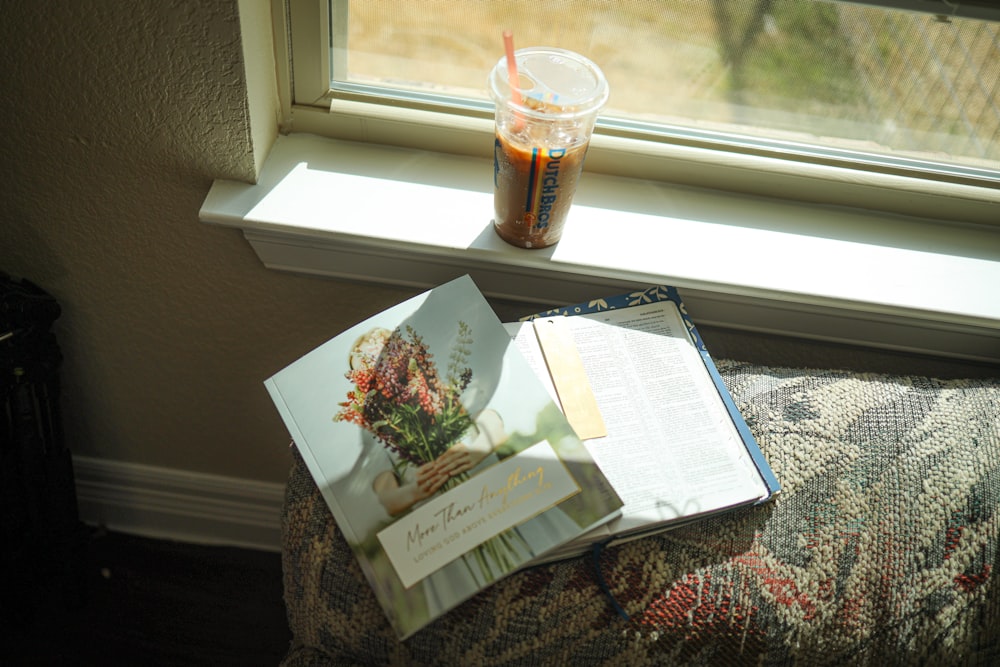 a book and a drink sitting on a chair by a window