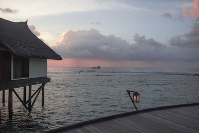 A cozy overwater bungalow glowing warmly at dusk, surrounded by calm ocean waters and palm trees.