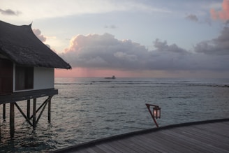 A cozy overwater bungalow glowing warmly at dusk, surrounded by calm ocean waters and palm trees.