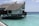 A thatched roof villa built on stilts over clear turquoise water. The villa has a wooden deck and traditional architecture. The ocean surrounding the structure is calm and vast, extending to the horizon under a partly cloudy sky.