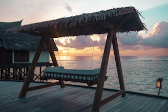A charming beachfront house with a wooden deck overlooking the ocean at sunset.
