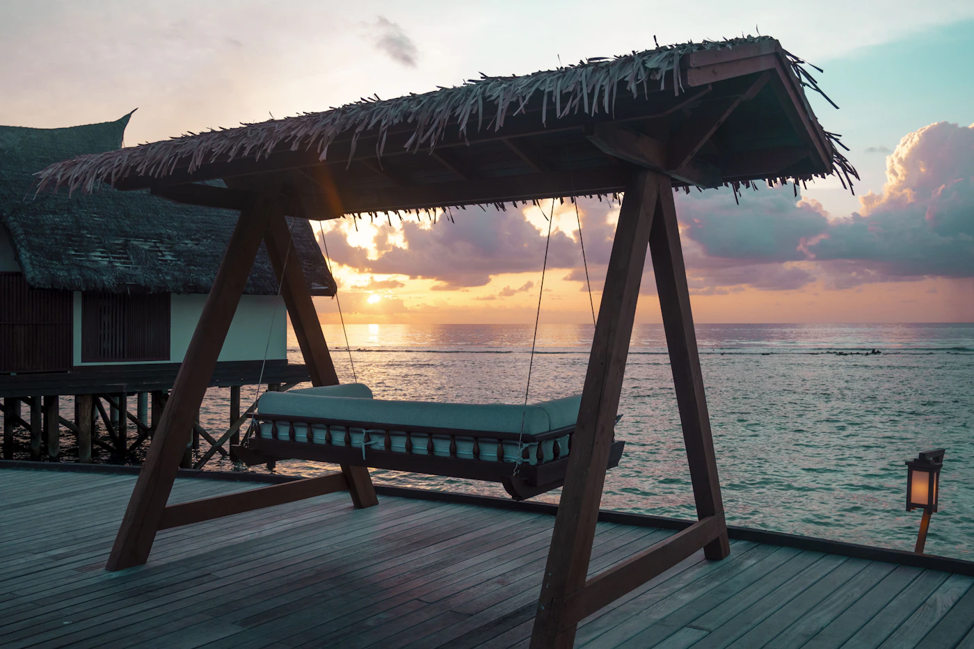 A shaded swing bed on a wooden terrace beside the sea.