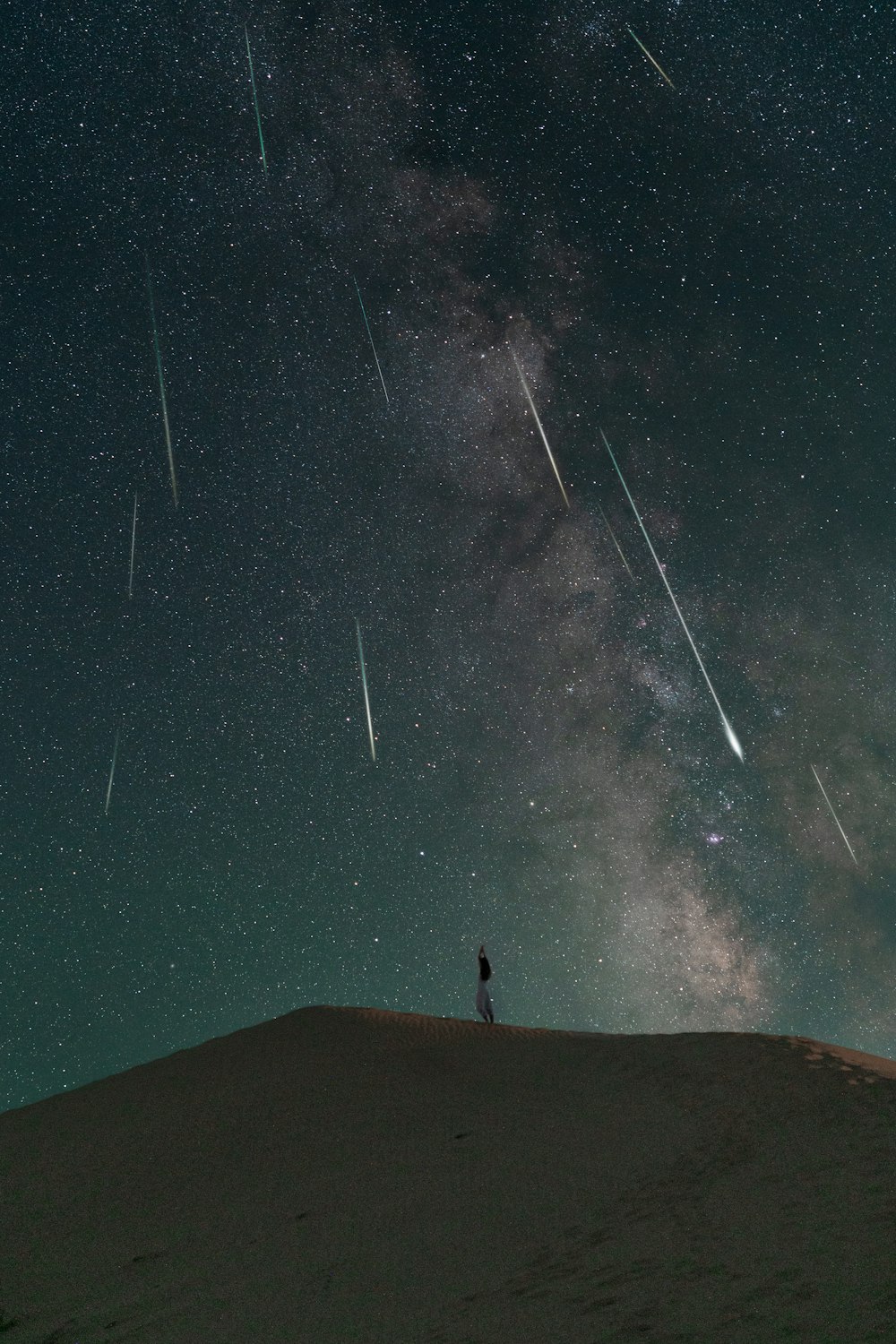 a person standing on top of a hill under a night sky filled with stars