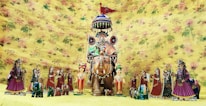 A collection of colorful, traditional Rajasthani puppets is displayed against a floral yellow background. The central figure is an elaborately decorated horse with a rider, surrounded by smaller human and animal figures, all adorned with traditional Rajasthani attire and accessories.