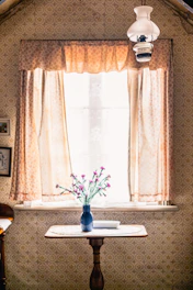 A cozy, sunlit room featuring a rustic wooden wardrobe next to a delicate glass table vase filled with fresh flowers.