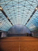 Bright indoor tennis court with polished wooden floor and clear net.