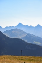 A peaceful landscape with a sunrise illuminating a cross on a hill.