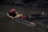 A person floats on calm water, wearing a red helmet and life jacket. The surrounding environment is dimly lit, suggesting an outdoor location with rocky edges.